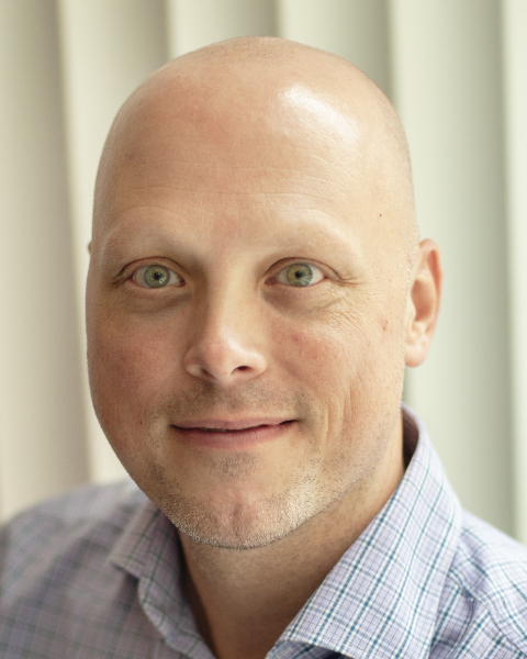 Cameron Popp Cameron Popp portrait looking at camera, wearing a plaid button-down shirt. Bald man with green eyes smiles slightly against a neutral backdrop.