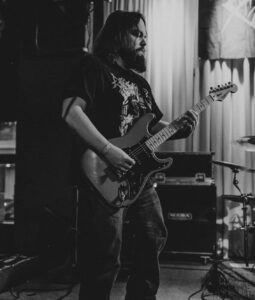 Matt Ibach, PMG's Senior Production Manager, playing electric guitar in a concert, black and white photo.